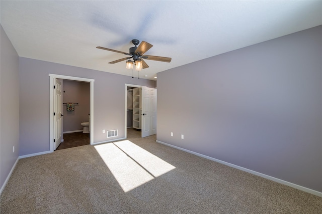 unfurnished bedroom featuring ensuite bathroom, carpet floors, a spacious closet, ceiling fan, and a closet