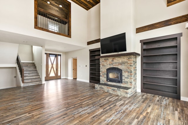 unfurnished living room featuring a towering ceiling, a fireplace, built in features, and dark hardwood / wood-style floors