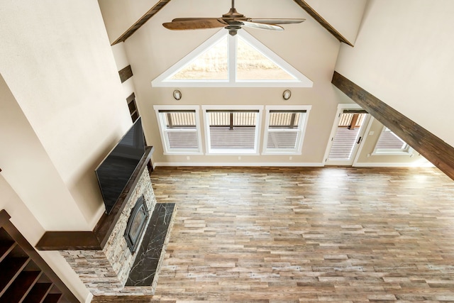 unfurnished living room featuring light hardwood / wood-style flooring, a fireplace, ceiling fan, and a high ceiling