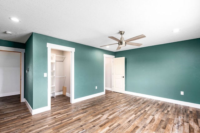 unfurnished bedroom with dark hardwood / wood-style flooring, a walk in closet, a closet, and ceiling fan