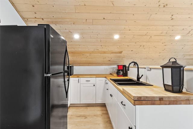 kitchen featuring butcher block counters, white cabinetry, a sink, and freestanding refrigerator