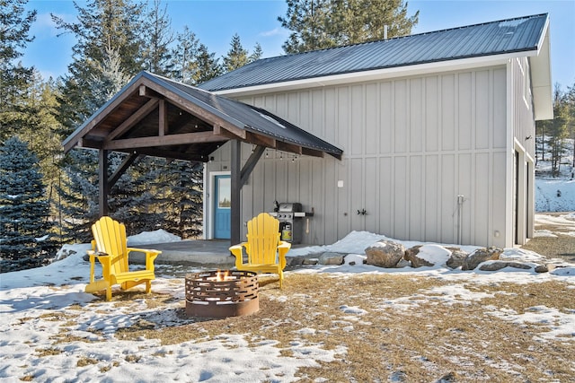 snow covered back of property with metal roof and an outdoor fire pit