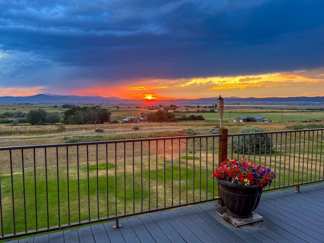 deck at dusk with a mountain view, a yard, and a rural view