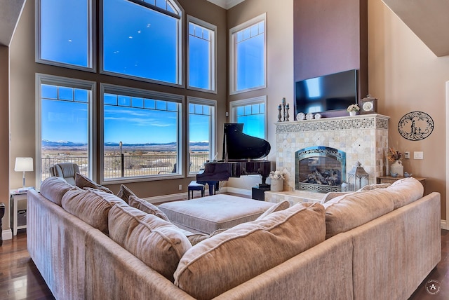 living room featuring a tiled fireplace, a towering ceiling, dark hardwood / wood-style floors, and a healthy amount of sunlight