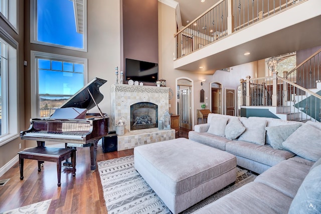 living room featuring a tile fireplace, wood-type flooring, plenty of natural light, and a high ceiling