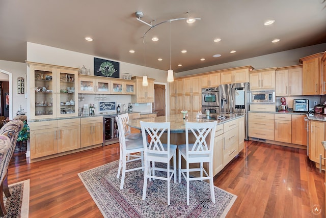 kitchen with appliances with stainless steel finishes, decorative light fixtures, an island with sink, beverage cooler, and light stone counters