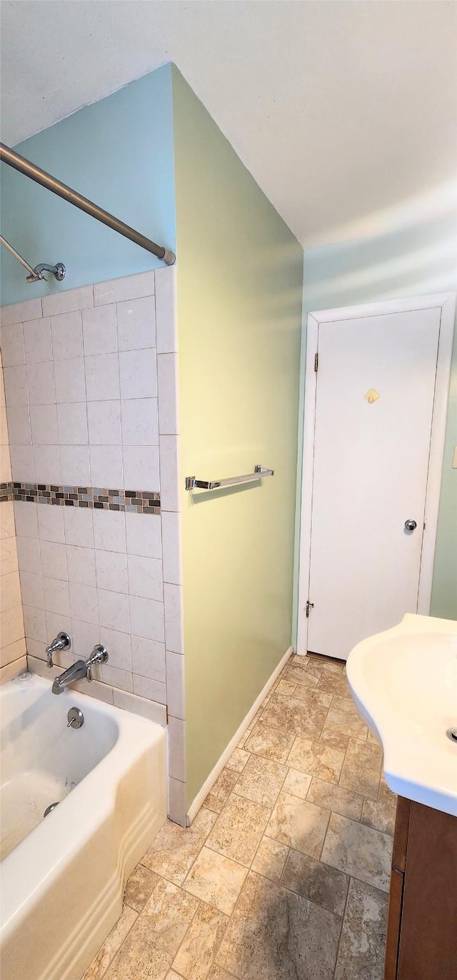 bathroom with vanity, vaulted ceiling, and tiled shower / bath