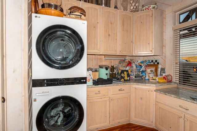 clothes washing area featuring cabinets and stacked washing maching and dryer