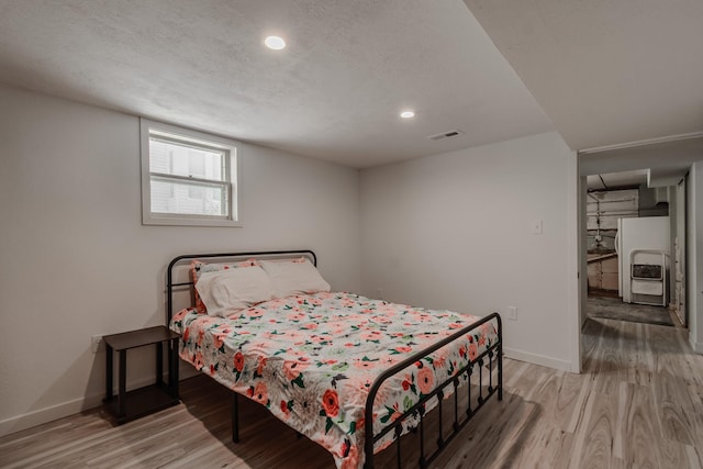 bedroom featuring hardwood / wood-style flooring, white fridge with ice dispenser, and a textured ceiling