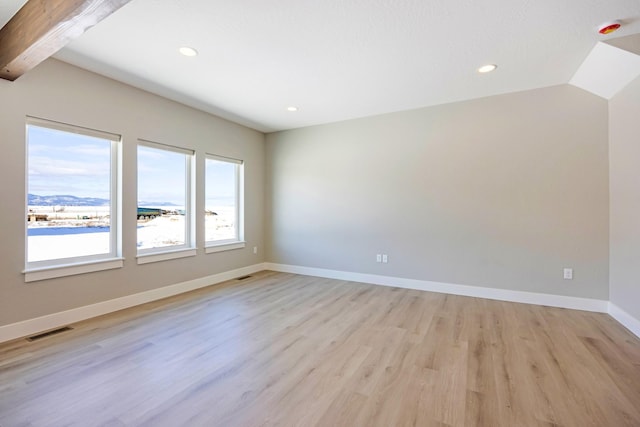 empty room featuring lofted ceiling with beams and light wood-type flooring