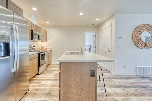 kitchen with sink, stainless steel appliances, a kitchen breakfast bar, light hardwood / wood-style floors, and a center island with sink