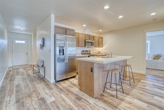 kitchen with stainless steel appliances, a kitchen island with sink, a breakfast bar area, and light wood-type flooring