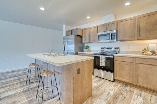 kitchen featuring a breakfast bar, an island with sink, sink, light hardwood / wood-style floors, and stainless steel appliances