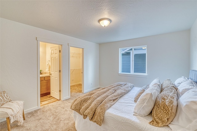 bedroom featuring light carpet, a walk in closet, a textured ceiling, and ensuite bathroom