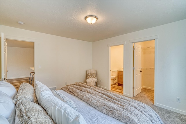 carpeted bedroom with a walk in closet, a textured ceiling, and ensuite bath