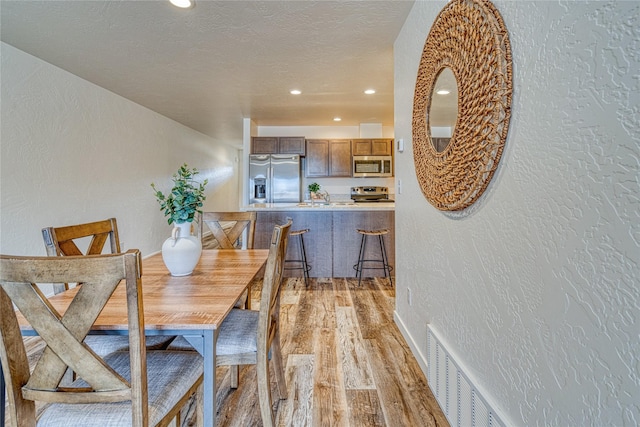 dining area with sink, light hardwood / wood-style floors, and a textured ceiling