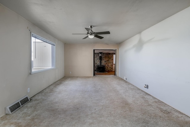 empty room featuring a wood stove, light colored carpet, and ceiling fan