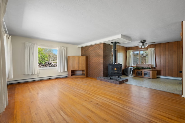 119 Fair St, Deer Lodge, MT 59722 - unfurnished living room featuring baseboard heating, plenty of natural light, a wood stove, and wood walls