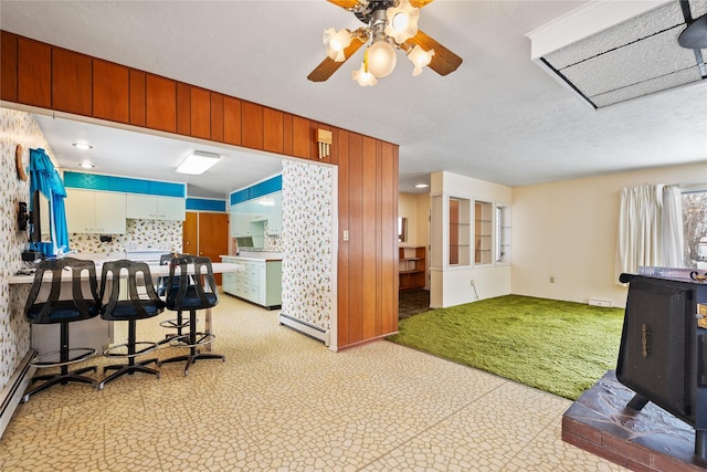 kitchen with ceiling fan, a baseboard heating unit, a kitchen breakfast bar, and wood walls