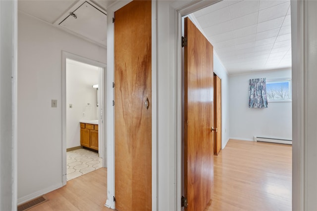 hallway with a baseboard heating unit and light hardwood / wood-style flooring