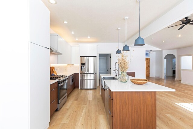 kitchen featuring decorative light fixtures, white cabinetry, a kitchen island with sink, stainless steel appliances, and light wood-type flooring