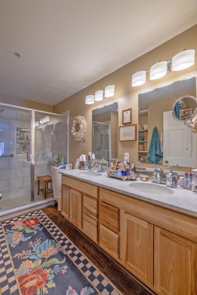 full bath with double vanity, a sink, wood finished floors, and a shower stall