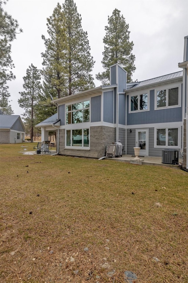 back of house with a standing seam roof, metal roof, central air condition unit, a yard, and a patio