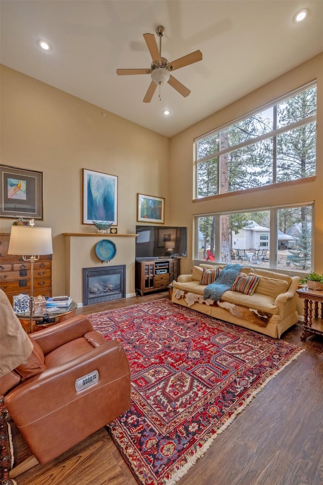living area with recessed lighting, a ceiling fan, a glass covered fireplace, and wood finished floors