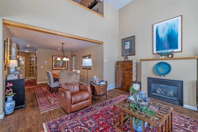 living area featuring an inviting chandelier, baseboards, a glass covered fireplace, and wood finished floors