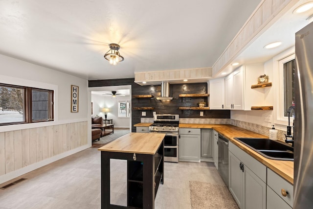 kitchen featuring gray cabinets, wooden walls, butcher block countertops, hanging light fixtures, and stainless steel appliances