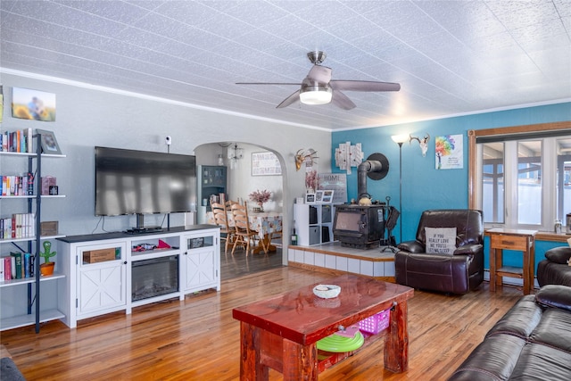 living room with hardwood / wood-style flooring, ceiling fan, crown molding, and a wood stove