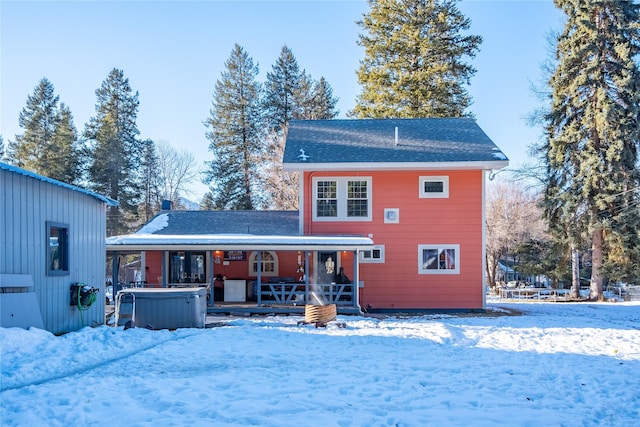 snow covered rear of property featuring a hot tub and covered porch