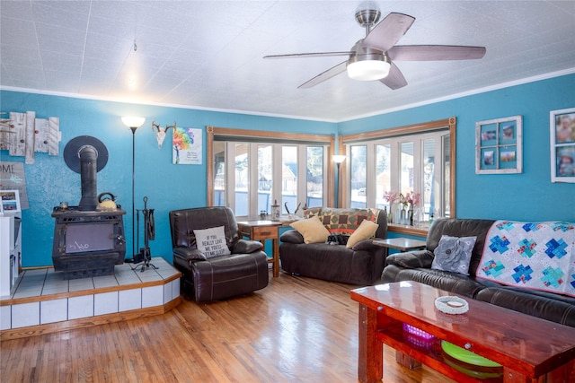 living room featuring wood-type flooring, a wood stove, crown molding, and ceiling fan