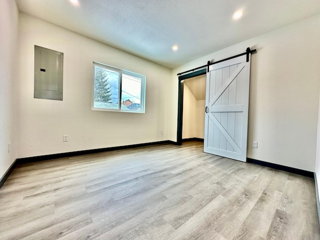 unfurnished bedroom featuring a barn door, electric panel, light hardwood / wood-style floors, and a textured ceiling