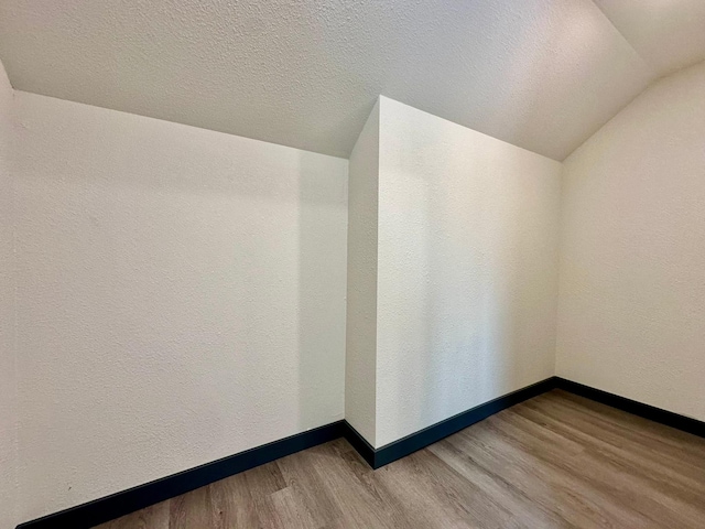 spare room featuring hardwood / wood-style flooring, vaulted ceiling, and a textured ceiling