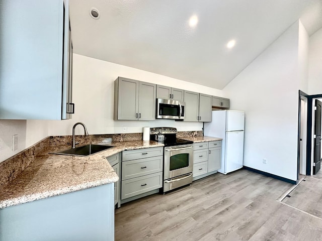 kitchen with sink, light stone counters, high vaulted ceiling, light wood-type flooring, and appliances with stainless steel finishes