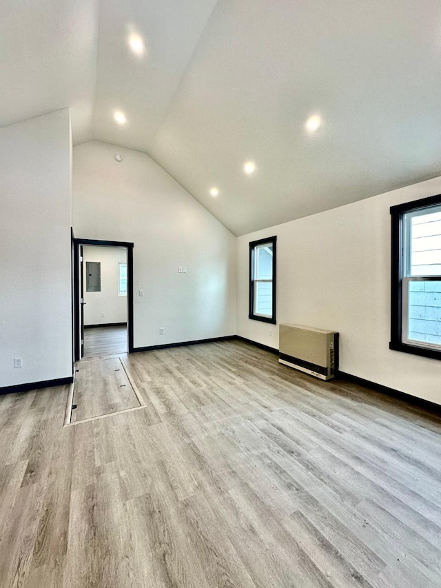 unfurnished room featuring lofted ceiling, radiator heating unit, and light wood-type flooring