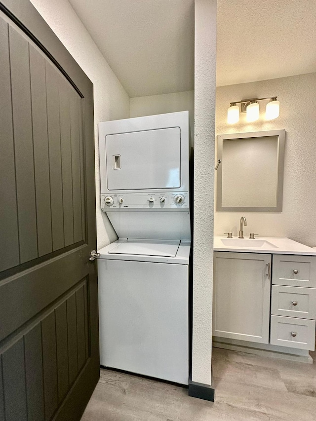 clothes washing area featuring stacked washer and dryer, sink, a textured ceiling, and light hardwood / wood-style flooring