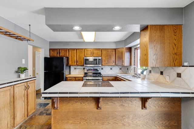 kitchen featuring a breakfast bar, tile countertops, sink, kitchen peninsula, and stainless steel appliances