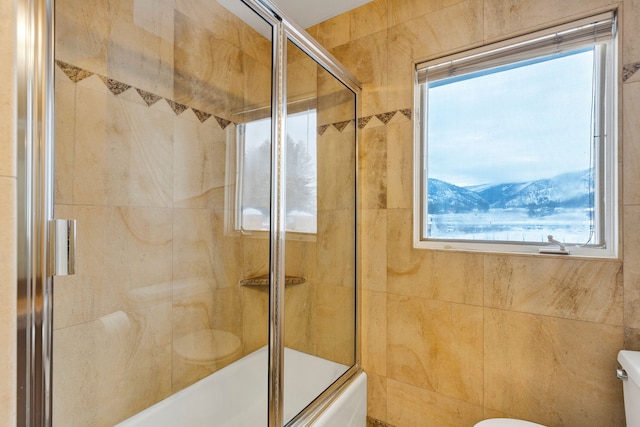 bathroom featuring shower / bath combination with glass door, toilet, and tile walls