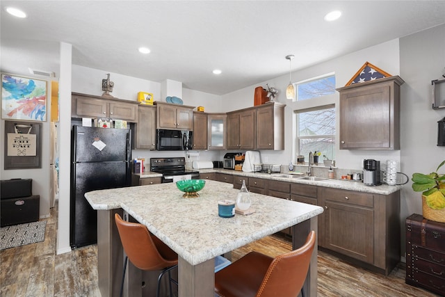 kitchen with sink, a breakfast bar area, a center island, hanging light fixtures, and black appliances