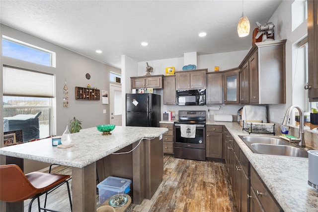 kitchen featuring pendant lighting, sink, black appliances, a kitchen island, and dark hardwood / wood-style flooring