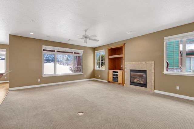 unfurnished living room with ceiling fan, light carpet, a textured ceiling, and a fireplace