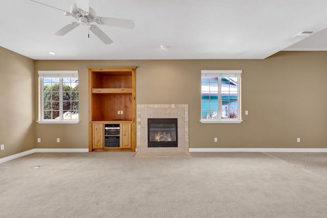 unfurnished living room featuring light carpet, a tiled fireplace, and ceiling fan