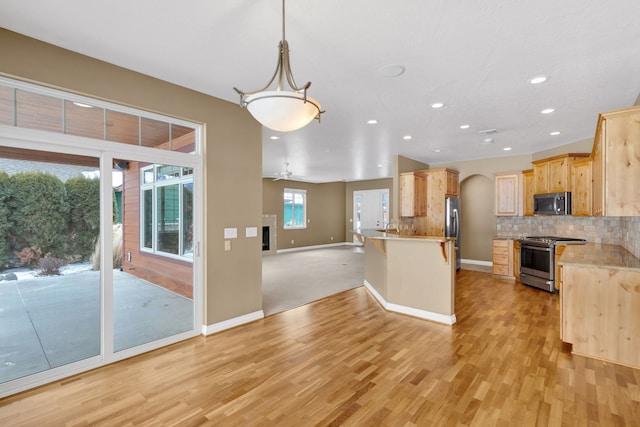 kitchen with light brown cabinetry, tasteful backsplash, decorative light fixtures, light wood-type flooring, and appliances with stainless steel finishes