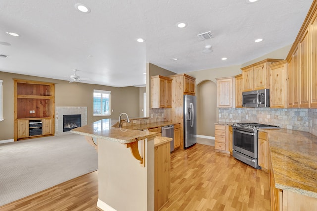 kitchen featuring a breakfast bar, a fireplace, kitchen peninsula, stainless steel appliances, and light brown cabinets