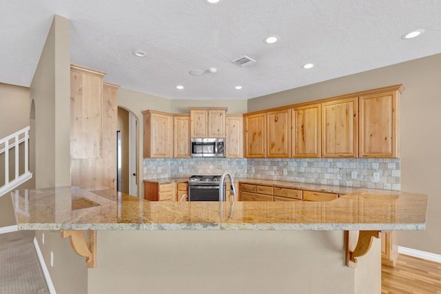 kitchen featuring appliances with stainless steel finishes, tasteful backsplash, light stone counters, a kitchen bar, and kitchen peninsula