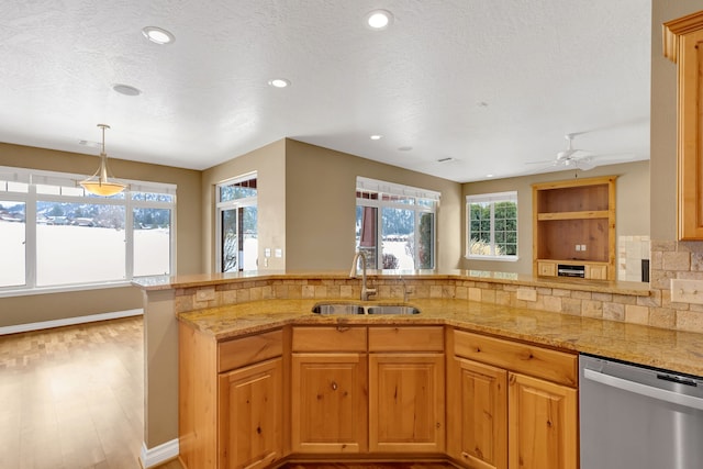 kitchen with sink, dishwasher, kitchen peninsula, light stone countertops, and backsplash