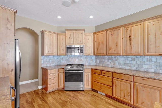 kitchen with stainless steel appliances, light stone countertops, light brown cabinets, and light hardwood / wood-style flooring