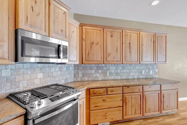 kitchen featuring appliances with stainless steel finishes, light brown cabinetry, tasteful backsplash, light hardwood / wood-style floors, and a textured ceiling